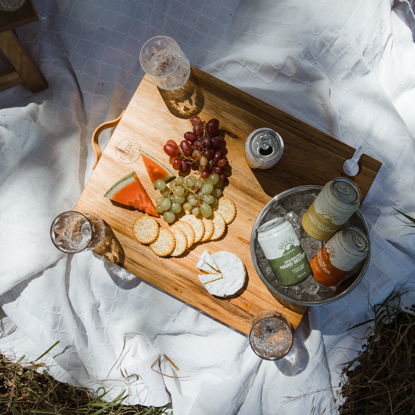 Picknicktisch mit Weingläser und Edelstahl Eiskübel aus Eichenholz welcher mit Champagner, Bier und Obst eingedeckt ist und im Freien steht