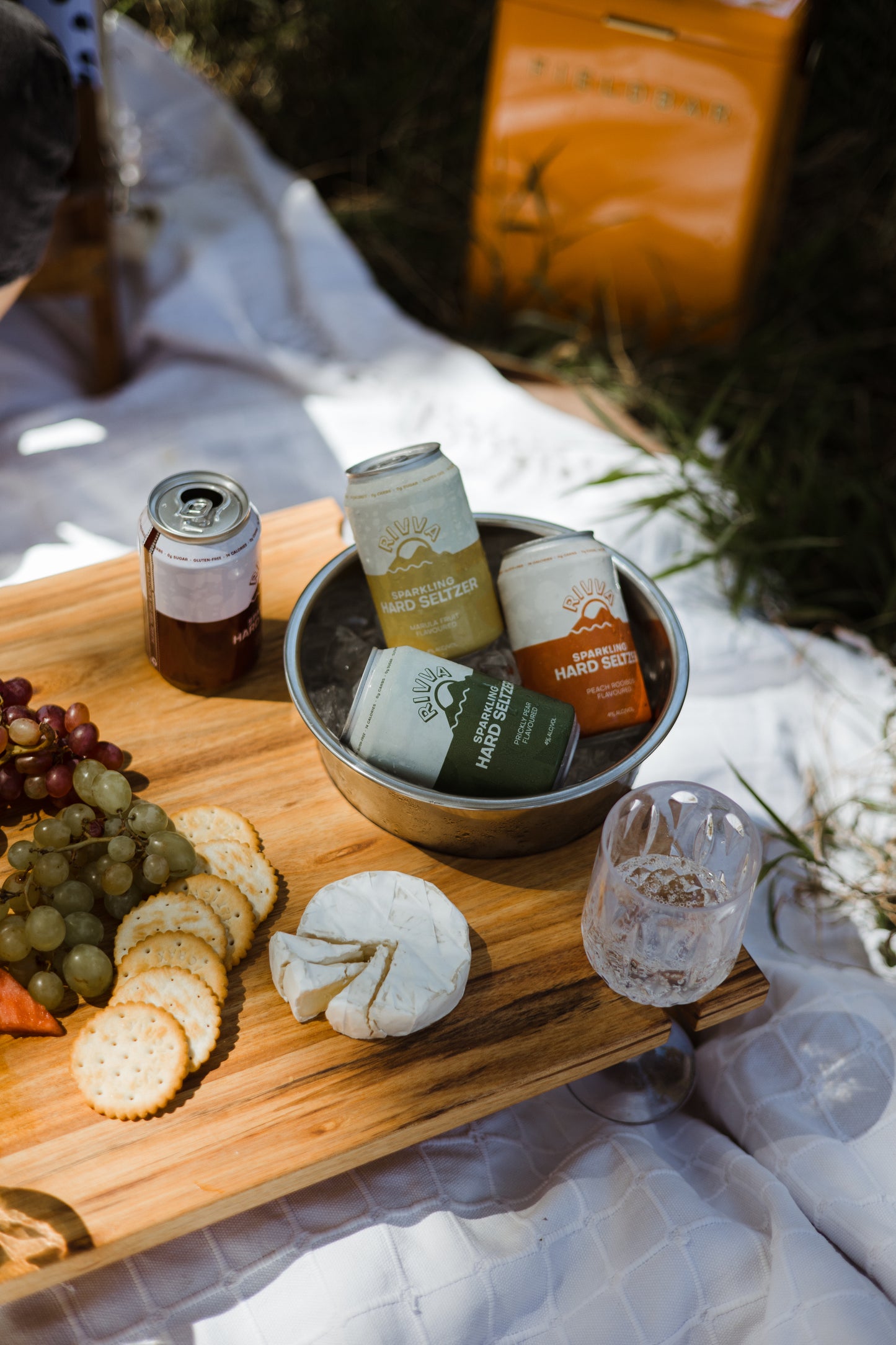 Picknicktisch mit Weingläser und Edelstahl Eiskübel aus Eichenholz welcher mit Champagner, Bier und Obst eingedeckt ist und im Freien steht