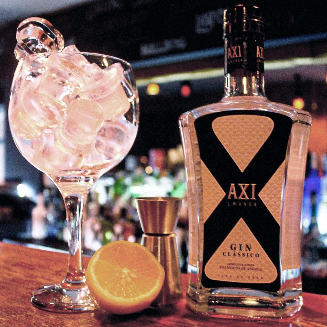 Axi Gin im Cocktailglas mit Eiswürfeln welcher auf einer Bar steht und mit Shaker und Zitrone umgeben ist