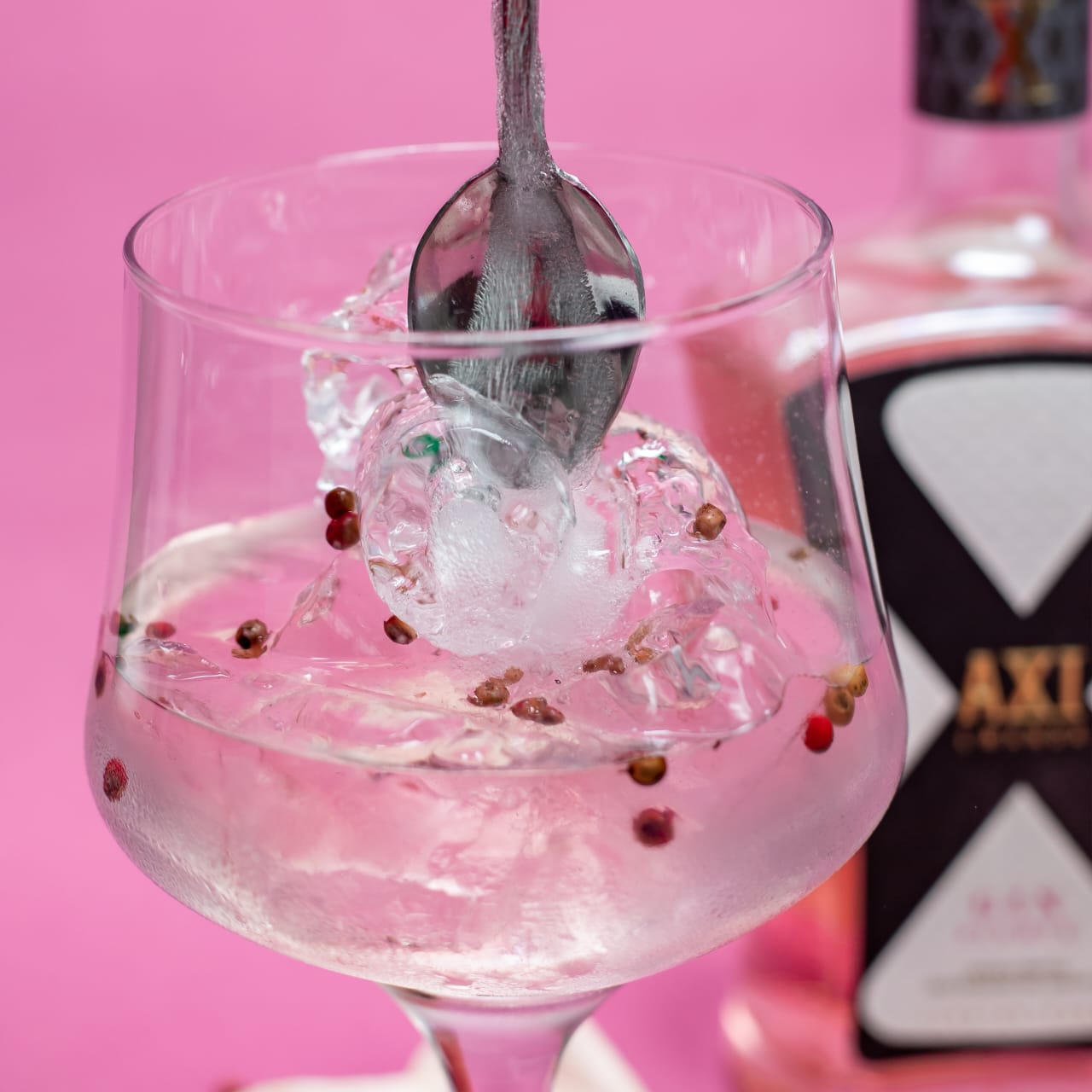 Axi Gin serviert im Glas mit Eiswürfeln und Gewürzen auf rosa Hintergrund.